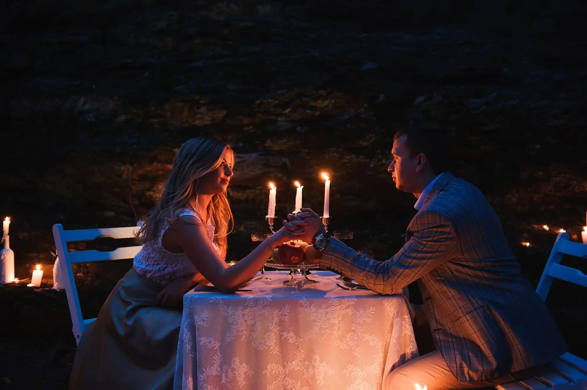 Romantic date night scene with a couple holding hands across a candlelit table outdoors