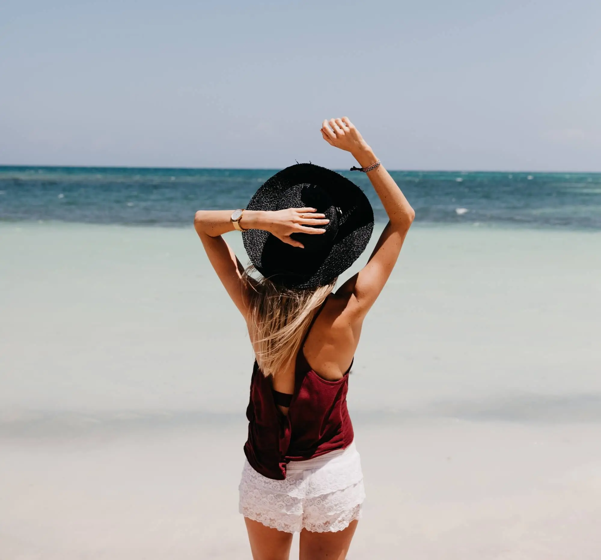 Traveler standing on a beach facing the ocean with a hat, symbolizing direct flights from Charlotte NC to spring travel destinations