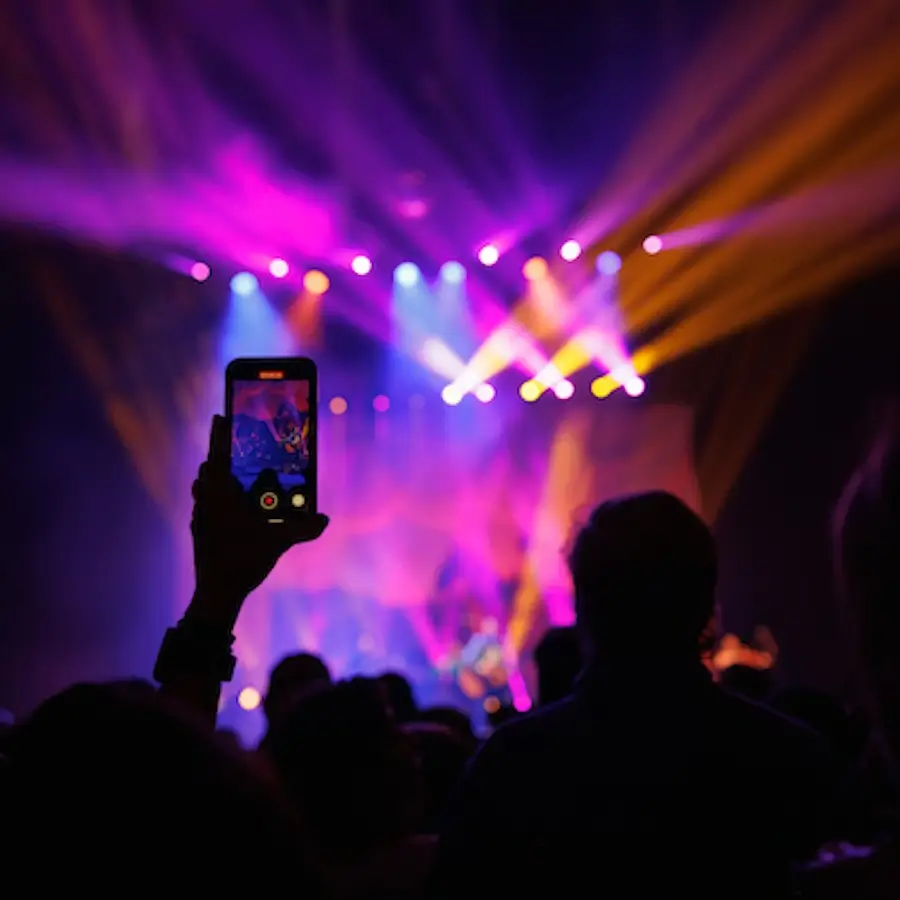 Person holding up a phone recording a concert with vibrant stage lighting and audience silhouettes