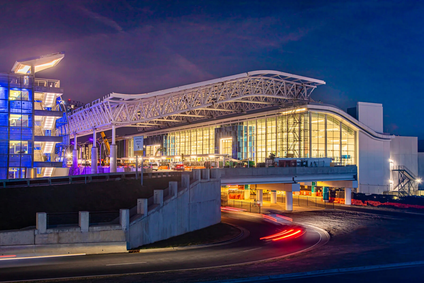 Modern airport terminal illuminated at night with streaking car lights.