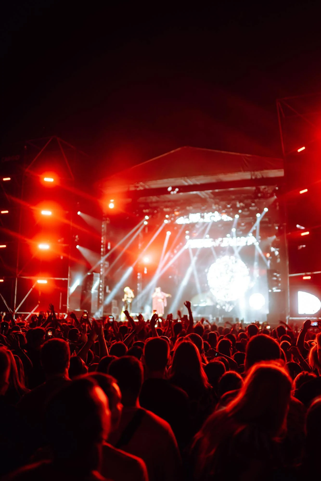 Concert audience under red stage lights with two performers on stage.