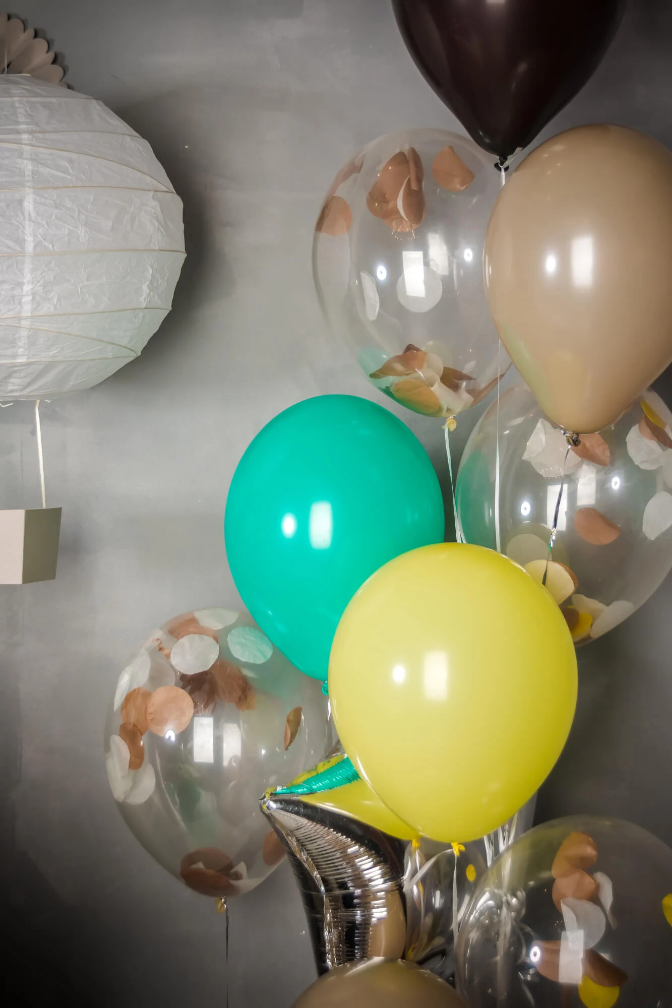 Colorful balloons with a paper lantern against a gray background.