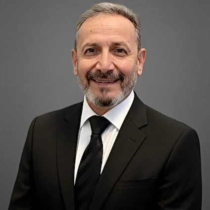 A man in a suit is smiling against a plain background, representing experienced staff from VOY Black Car.