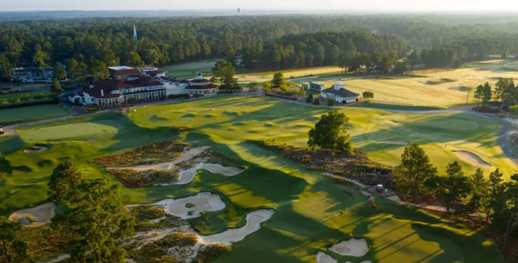 Aerial view of a golf course with sand traps, green lawns, and a clubhouse surrounded by trees.