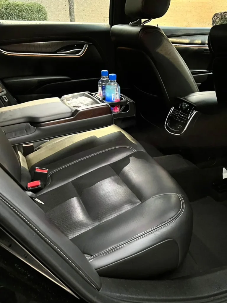 Luxurious black leather interior of an executive sedan with rear armrest, cup holders, and bottled water.