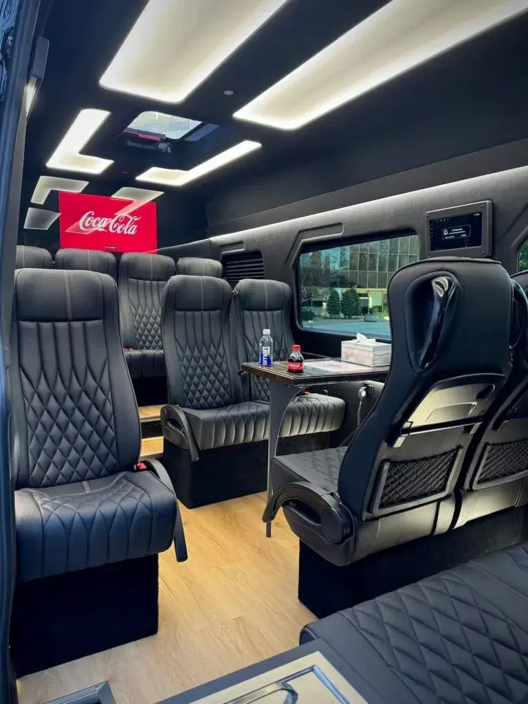 Luxurious Executive Sprinter Van interior with quilted leather seats, overhead lighting, and a small table.