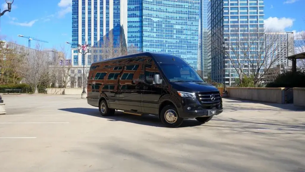 Black executive Sprinter van parked in an urban area with tall buildings in the background.