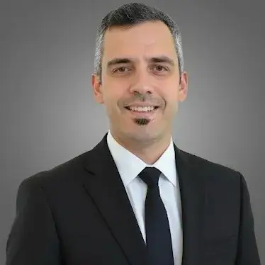 Man in a suit and tie smiling against a gray background.