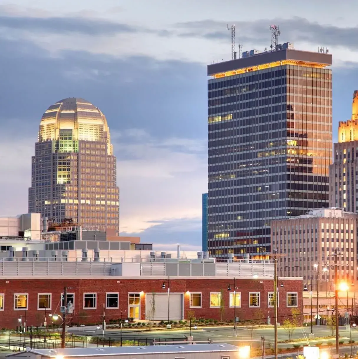 Cityscape of Winston-Salem, featuring modern skyscrapers with a sunset sky.
