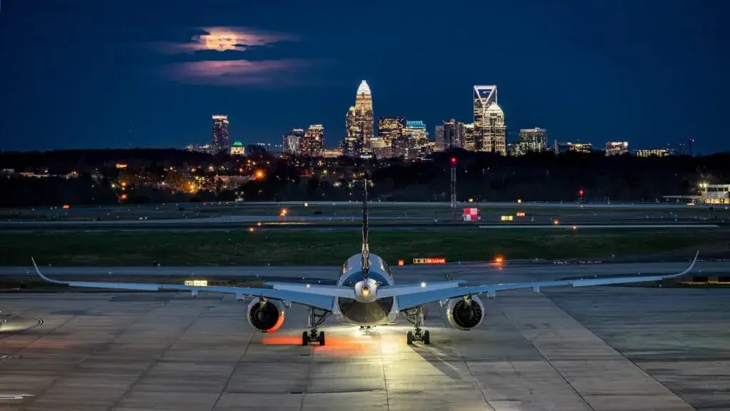 Airplane on tarmac at night with city skyline and moon in background.