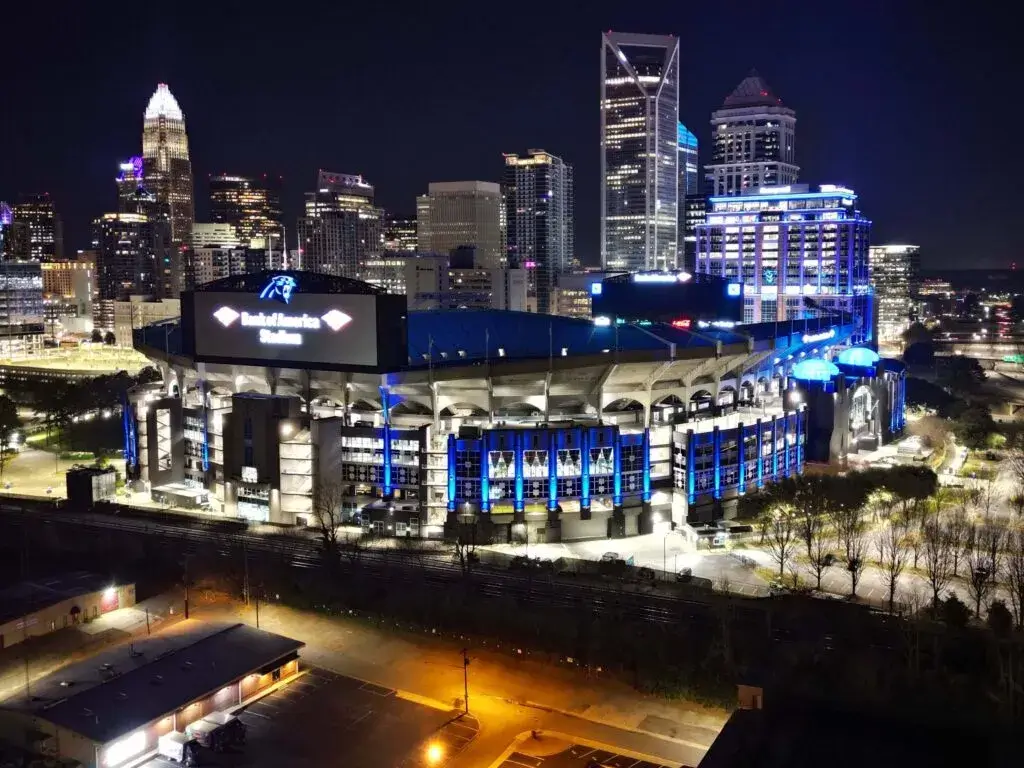 City skyline at night with a large stadium in the foreground illuminated in blue lights.