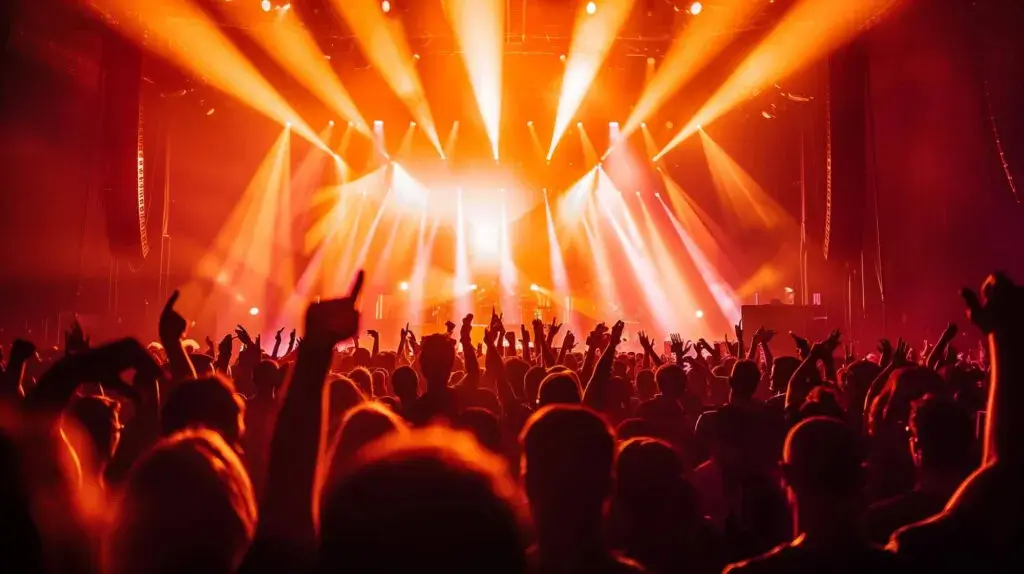 Concert crowd with raised hands surrounded by vibrant orange stage lighting.